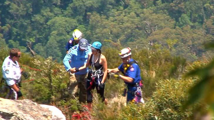 The young woman involved in the abseiling accident is led from the bush by rescuers.