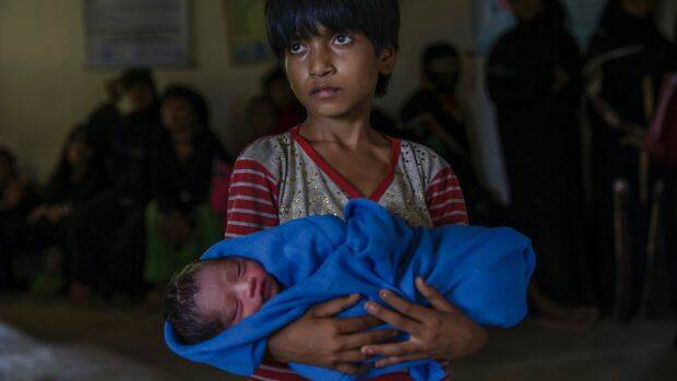 Rohingya girl Afeefa Bebi, who crossed over from Myanmar into Bangladesh, holds her few-hours-old brother as doctors check her mother Yasmeen Ara at a community hospital in Kutupalong refugee camp. Photo: AP